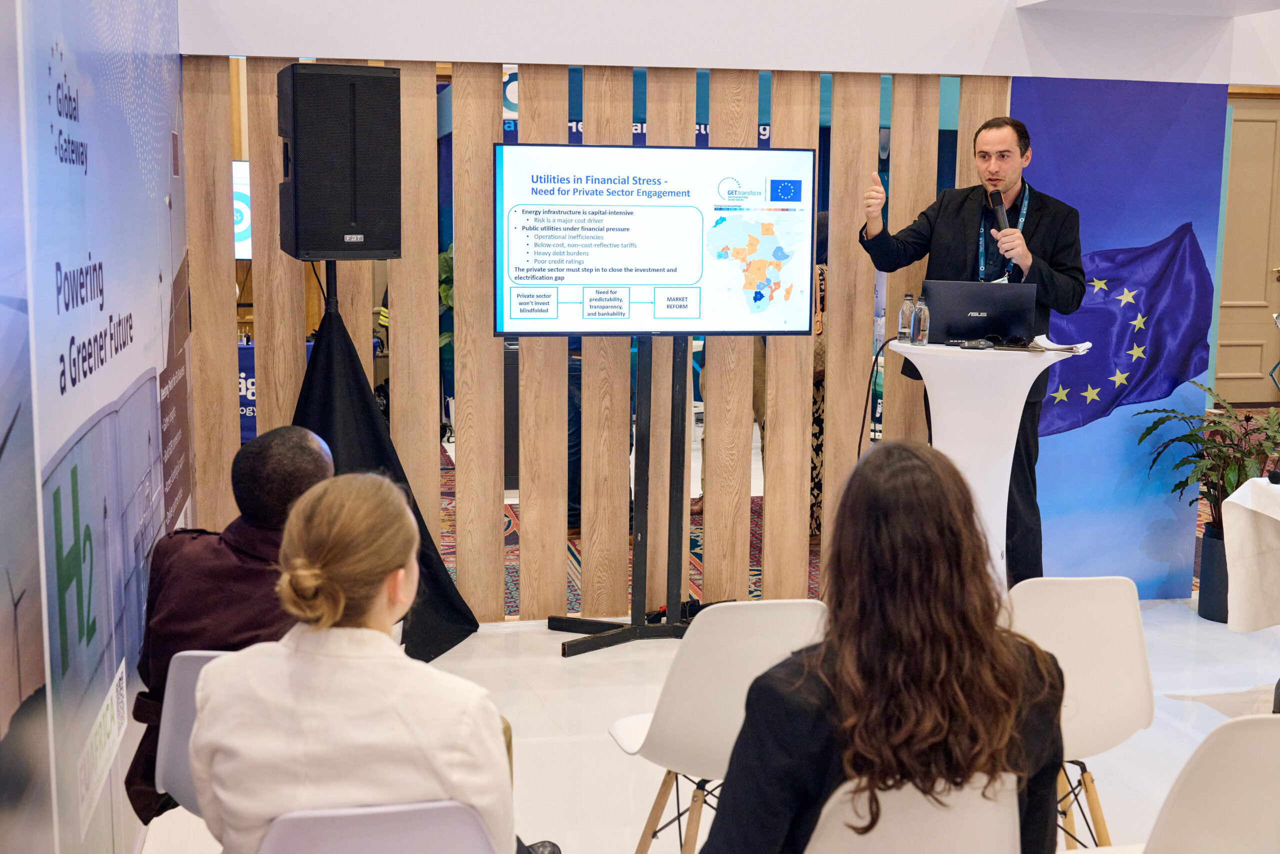 Presentation ongoing at the European Union pavilion, while a small audience watches. The screen shows a map of Europe and Africa and text about private sector engagement.
